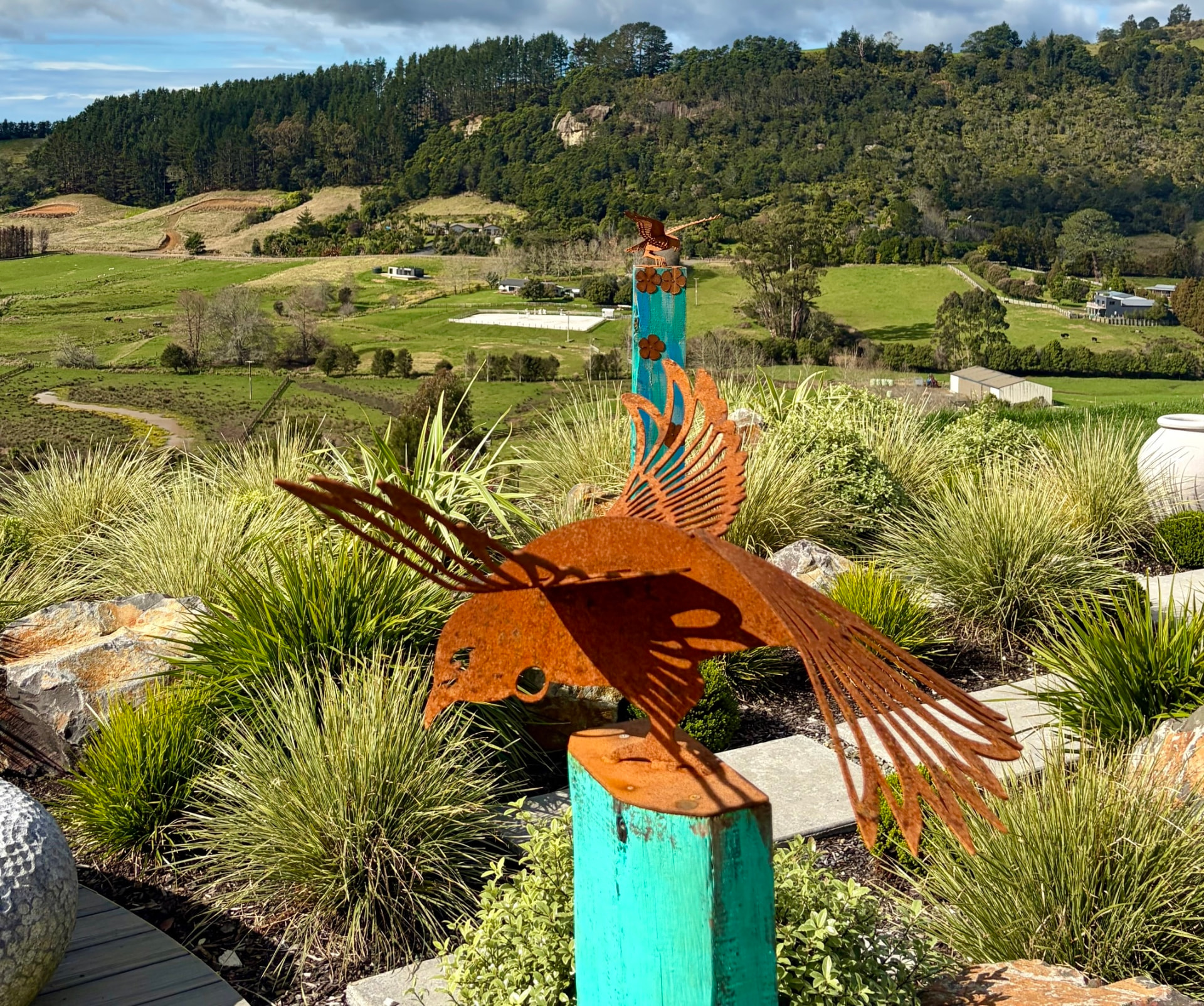 Rust metal bird sculptures among grasses overlooking the Coroglen valley